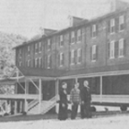 Three people standing in front of a large wooden building in a rural setting.