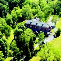 A large house surrounded by dense green trees and lawns.