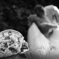 Black and white photo of a wedding bouquet with a bride and groom blurred in the background.